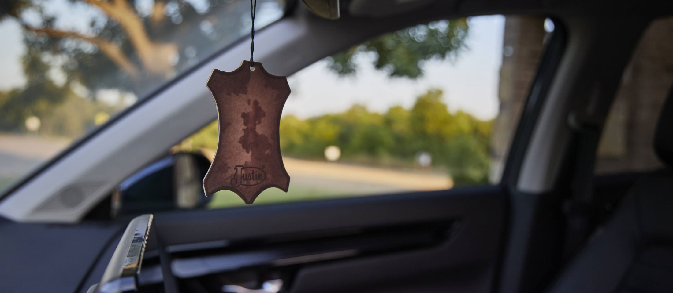 A Justin Air Freshener hanging from a car mirror.